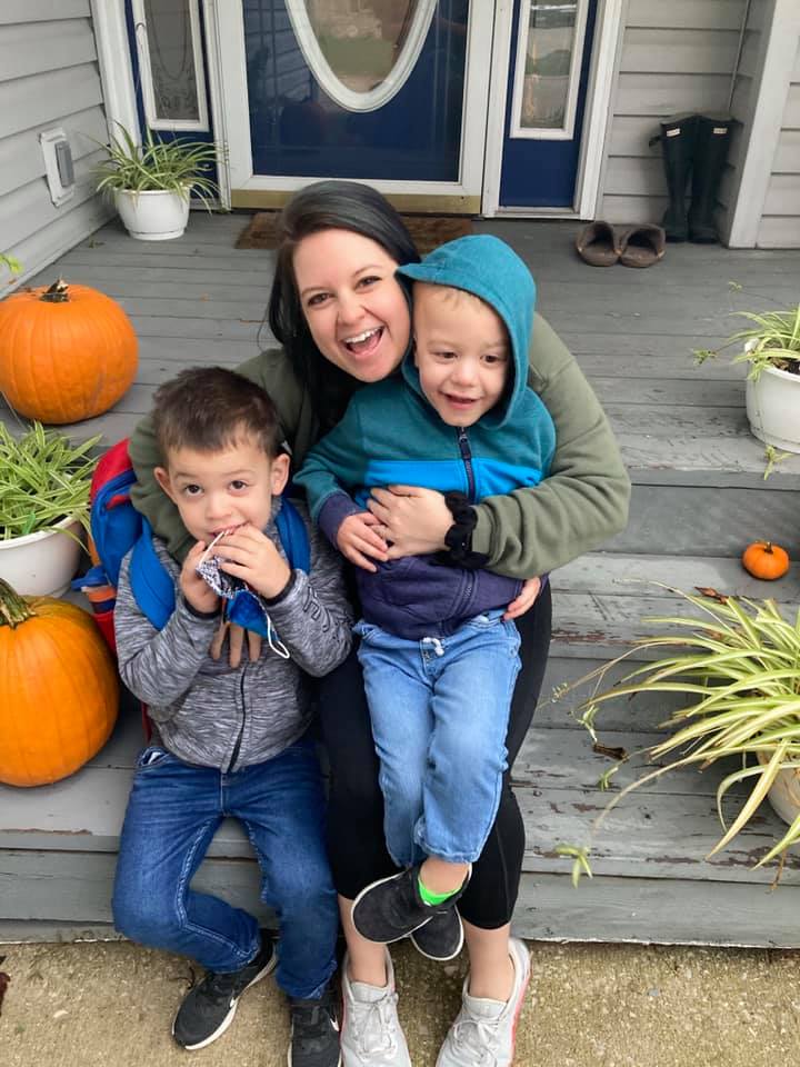 Woman with two young boys in coats sitting on porch with pumpkins