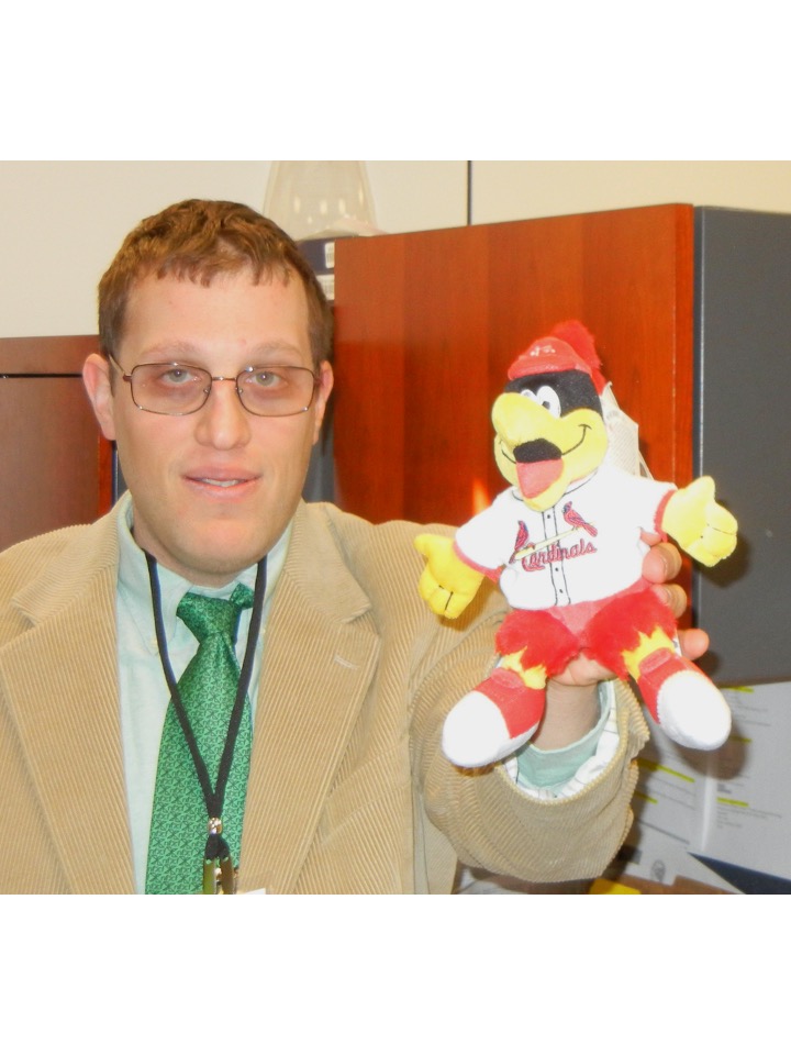Man with glasses in suit and tie holding a puppet of St. Louis Cardinals baseball mascot Fredbird